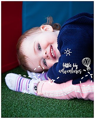 A toddler aged girl bends her head to her toes while grinning at the Little Big Adventures photographer