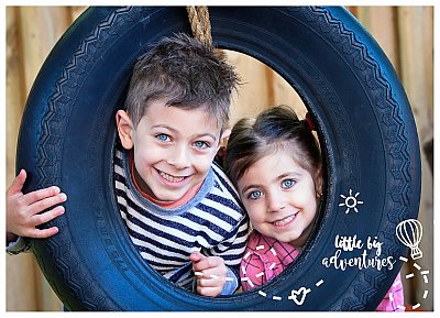 An older brother and his younger sister girn while looking through a suspended tyre window together at the Little Big Adventures Childcare Photographer