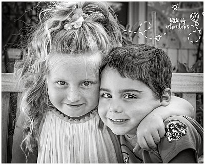 Two siblings hug and smile adorably at the camera.  The image is tastefully and timelessly rendered in black and white.  Photo by Little Big Adventures Photography
